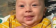 Jacob Ap is registered to the contest to win money with this photo: baby, child, smiling, tongue_out, yellow_shirt, toy, hand, face, dimples, bald_head, colorful, fabric, patterned, infant, cute, playful, indoors, closeup, person, happy