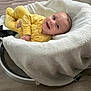 baby, smiling, yellow_outfit, blanket, baby_rocker, wooden_floor, happy, infant, cozy, indoor, child, cute, face, person, clothing, resting, soft, comfort, portrait, young