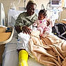 hospital, patient, baby, elderly_person, hospital_bed, medical_equipment, yellow_cast, blanket, pajamas, child, adult, monitor, bed, window, chair, tubes, hospital_gown, person, room, care