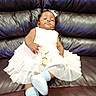 baby, child, dress, white_dress, number_5, sitting, leather_couch, couch, footwear, socks, baby_shoes, headband, earrings, indoor, celebration, portrait, sleepy, child_portrait, person, infant