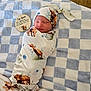 baby, newborn, infant, swaddle, hat, sleeping, blanket, checkered_blanket, wood_floor, milestone_card, animal_print, cow_pattern, teddy_bear, cozy, portrait, nursery, soft_texture, peaceful, adorable, cute