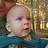 baby, child, infant, adult, face, portrait, close_up, blue_eyes, wide_eyed, outdoors, forest, trees, sunlight, nature, sitting, being_held, green_clothing, watch, mesh_screen, family
