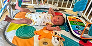 Vito-Lucciano participe au concours pour gagner de l'argent avec cette photo : baby, infant, playmat, toy, colorful, soft_toy, crib, leg_up, cute, lying_down, patterned_clothing, floor, indoor, child, newborn, play_area, baby_gym, expression, small, human