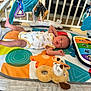 baby, infant, playmat, toy, colorful, soft_toy, crib, leg_up, cute, lying_down, patterned_clothing, floor, indoor, child, newborn, play_area, baby_gym, expression, small, human