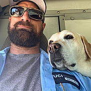 Burlie joined the competition — help win amazing prizes! man, beard, sunglasses, cap, dog, golden_retriever, pet, animal, portrait, selfie, indoor, shirt, uniform, badge, vehicle, companion, relaxed, casual, friendship, closeup