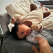 Angel is registered to the contest to win money with this photo: baby, infant, couch, blanket, pillow, gloves, socks, hand, indoor, furniture, soft_texture, curious, laying_down, cozy, child, person, home, relaxing, cute, interaction