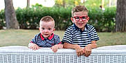 Alex a rejoint le concours — aidez-le/la à gagner de superbes lots ! child, children, boy, toddler, glasses, striped_shirt, outdoor, garden, greenery, wicker_fence, smiling, curious, cute, portrait, summer, siblings, nature, happy, casual_clothing, daylight