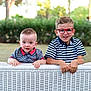 child, children, boy, toddler, glasses, striped_shirt, outdoor, garden, greenery, wicker_fence, smiling, curious, cute, portrait, summer, siblings, nature, happy, casual_clothing, daylight