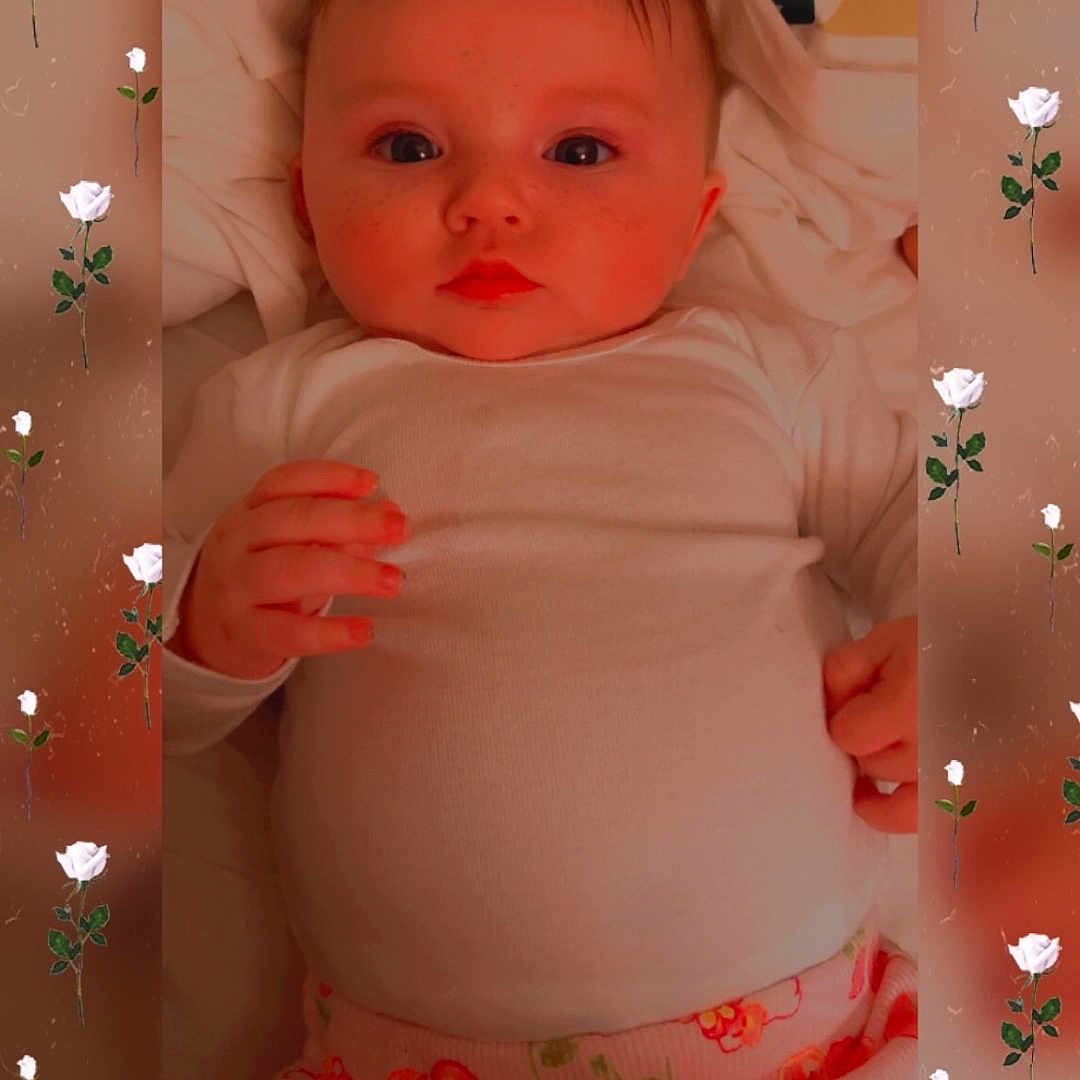 Heather joined the competition — help win amazing prizes! baby, infant, white_shirt, floral_pants, lying_down, cute, face, hands, roses, frame, pattern, soft, cozy, portrait, child, young_baby, indoors, blanket, skin, expression