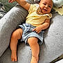Léo participe au concours pour gagner de l'argent avec cette photo : baby, child, smiling, cushion, clothing, yellow_top, blue_shorts, skin, foot, leg, arm, furniture, indoor, soft_texture, cute, happy, person, relaxing, infant, comfort