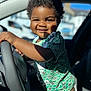 child, toddler, smiling, curly_hair, steering_wheel, car_interior, sunlight, portrait, happy, green_shirt, shorts, seat, window, daylight, closeup, baby, person, casual_clothing, indoor, cute