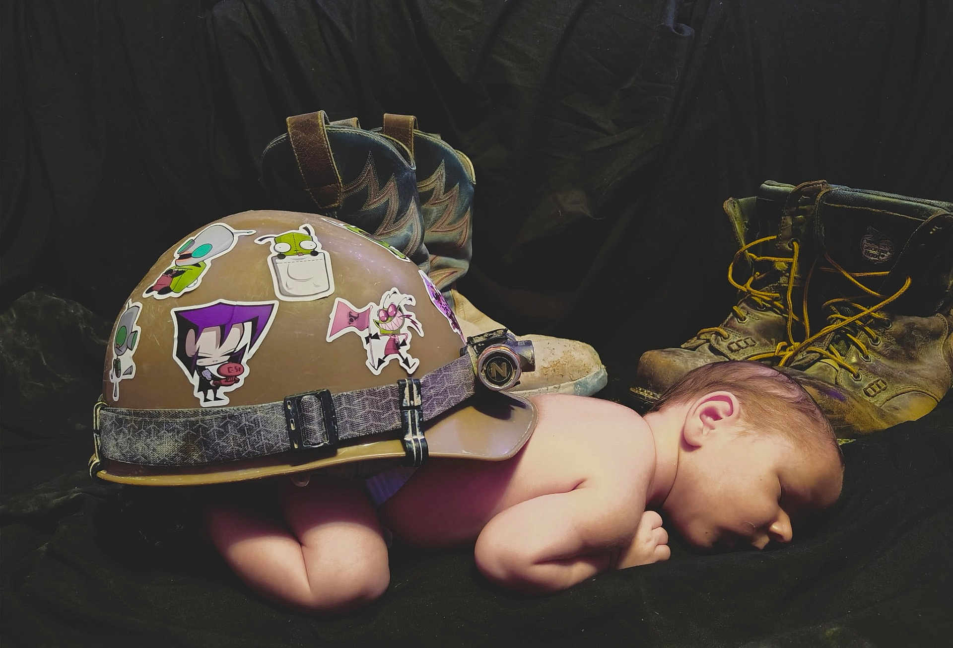 Ridge is registered to the contest to win money with this photo: baby, sleeping, helmet, stickers, boots, work_boots, bare_skin, infant, rest, cute, hard_hat, child, footwear, protection, contrast, peaceful, studio, dark_background, side_profile, newborn