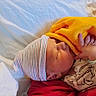 newborn, baby, infant, sleeping, bed, blanket, hat, striped_hat, pajamas, onesie, hand, face, portrait, indoors, cozy, bedding, soft_blanket, yellow_blanket, red_clothing, resting