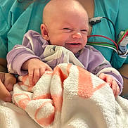 Melody joined the competition — help win amazing prizes! baby, blanket, person, clothing, hand, medical_equipment, scrubs, smile, face, infant, holding, indoor, cute, human, newborn, expression, skin, curly_hair, hospital, comfort