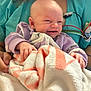 baby, blanket, person, clothing, hand, medical_equipment, scrubs, smile, face, infant, holding, indoor, cute, human, newborn, expression, skin, curly_hair, hospital, comfort