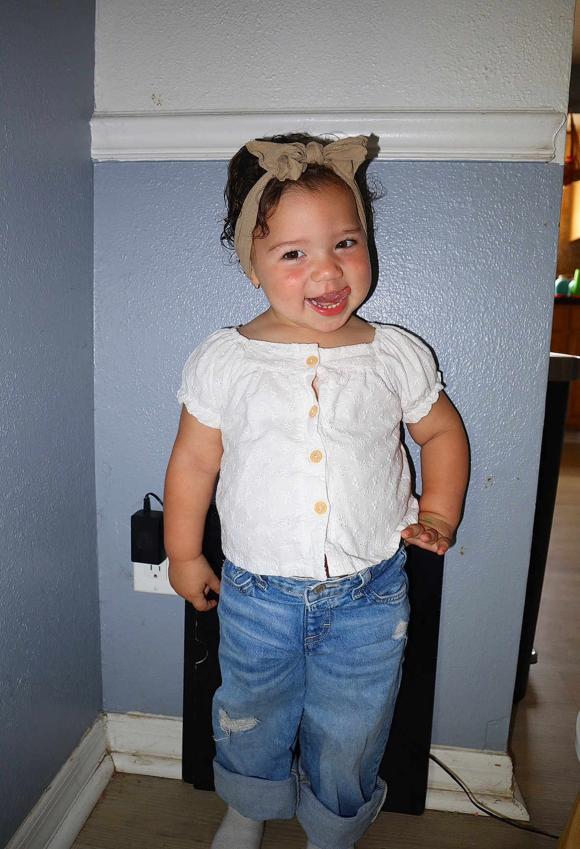 Maeve joined the competition — help win amazing prizes! toddler, child, smiling, headband, white_blouse, blue_jeans, rolled_jeans, standing, indoor, wall, floor, power_outlet, playful, cute, person, portrait, happy, short_hair, casual_clothing, home