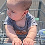 Nathaniel is registered to the contest to win money with this photo: baby, child, shopping_cart, hands, onesie, outdoor, curious, infant, grip, face, head, skin, short_hair, person, cute, daylight, expression, casual_clothing, closeup, young
