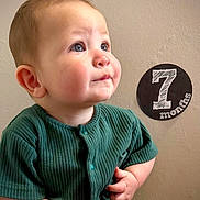 Riot joined the competition — help win amazing prizes! 7_months, baby, cheeks, child, curious, cute, expression, eyes, face, green_clothing, hand, indoor, infant, milestone, portrait, ribbed_fabric, sitting, skin, texture, wall