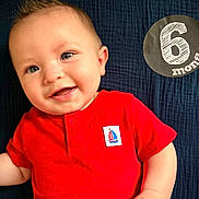 Riot joined the competition — help win amazing prizes! baby, infant, smiling, red_shirt, milestone, 6_months, cute, portrait, child, lying_down, face, happy, close_up, skin, hand, blue_background, texture, young_child, casual_clothing, one_person