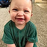 baby, child, smiling, green_clothing, ribbed_fabric, carpet, indoor, toy, happy, face, hair, spiky_hair, person, infant, cute, sitting, floor, home, furniture, car_seat