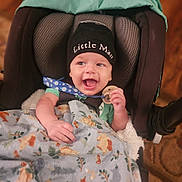 Ezekiel joined the competition — help win amazing prizes! baby, infant, smiling, hat, blanket, car_seat, toy, child, happy, clothing, face, headwear, indoor, person, closeup, cute, warm_lighting, seat_belt, pattern, wooden_toy