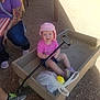 toddler, child, wagon, pink_hat, pink_shirt, shorts, shoes, adult, tattoos, purple_shirt, picnic_table, checkered_tablecloth, outdoor, gravel, sunlight, shadow, plastic_bag, yellow_bottle, handle, seated