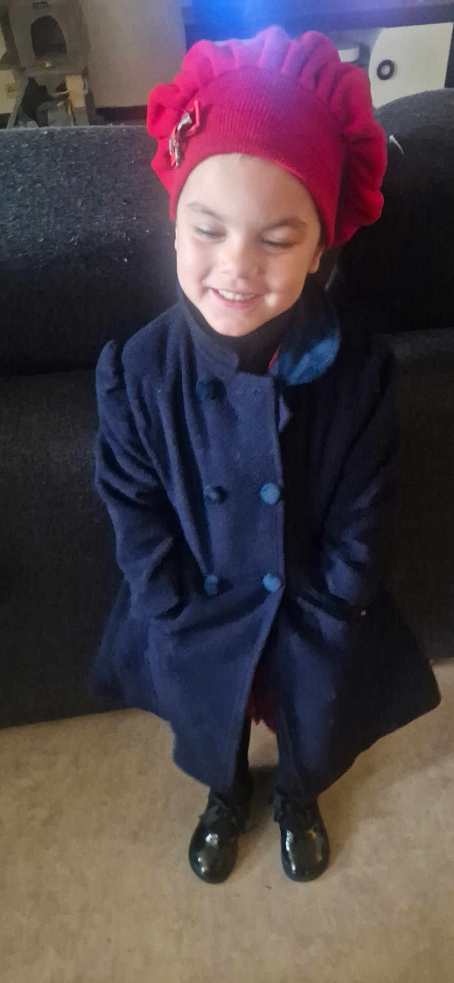Aaliyah a rejoint le concours — aidez-le/la à gagner de superbes lots ! child, smiling, red_hat, coat, black_shoes, indoor, living_room, furniture, couch, floor, person, portrait, clothing, happy, headwear, shoes, fashion, cute, young, standing