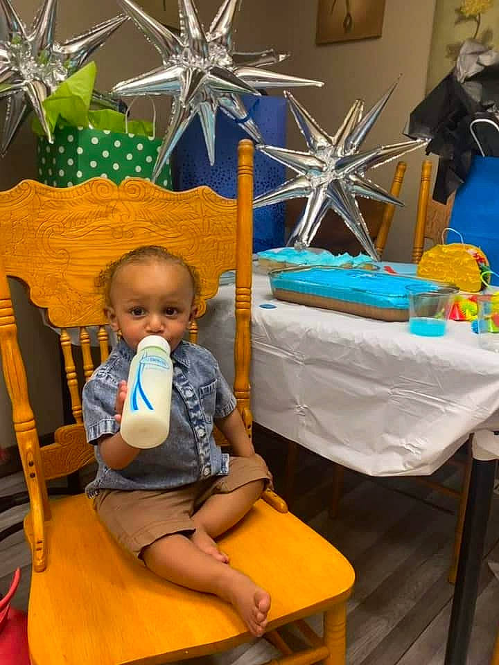 Malik is registered to the contest to win money with this photo: baby, baby_products, blue, chair, child, comfort, event, fun, leisure, linens, person, picture_frame, room, shorts, sitting, t_shirt, table, toddler, vacation, visual_arts