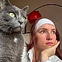 cat, close_up, domestic_animal, feline, fur, gray_cat, green_eyes, headband, indoor, looking_away, natural_light, pet, portrait, red_lamp, resting_chin, thoughtful, whiskers, white_shirt, woman, wooden_ceiling