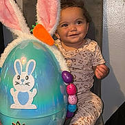 Soraya joined the competition — help win amazing prizes! toddler, child, smiling, chair, pajamas, leopard_print, curly_hair, easter_egg, bunny_ears, carrot, colorful_eggs, indoor, wall, foot, cute, happy, holiday, celebration, toy, seat