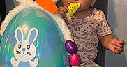 Soraya is registered to the contest to win money with this photo: toddler, child, toy, easter_egg, bunny_ears, carrot, colorful_eggs, chair, indoor, curious, playful, pajamas, cute, baby, person, smiling, decorations, holiday, seat, young_child