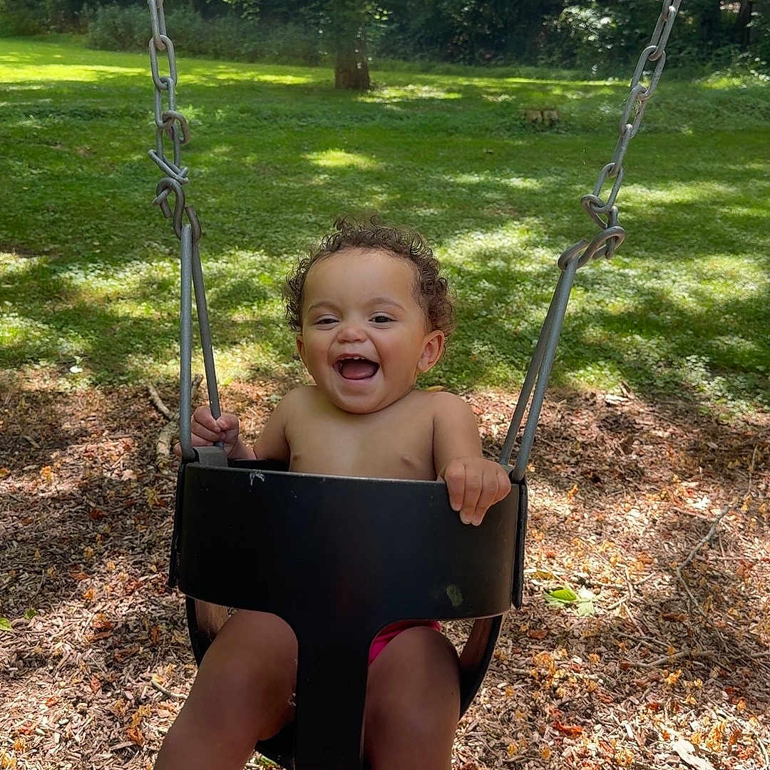 Soraya joined the competition — help win amazing prizes! toddler, child, swing, playground, outdoor, park, happy, smiling, curly_hair, barefoot, sunlight, nature, trees, grass, wood_chips, summer, fun, joy, baby, daytime