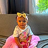 Soraya is registered to the contest to win money with this photo: birthday, child, clothing, couch, curly_hair, cute, daylight, face, gold_bow, greenery_outside, headband, holding_object, indoor, person, pink_tutu, portrait, sitting, toddler, white_shirt, window