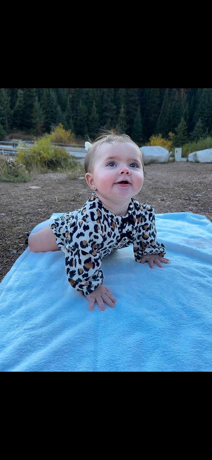 Zaylee joined the competition — help win amazing prizes! baby, infant, crawling, leopard_print, blue_blanket, outdoors, forest, pine_trees, rocks, dirt_ground, smiling, hands, cheeks, bow, onesie, eyes, nature, toddler, portrait, playful