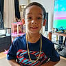 Shyden is registered to the contest to win money with this photo: child, boy, superman_shirt, gold_chain, smile, indoor, living_room, toy, television, furniture, carpet, lamp, curtain, table, speaker, person, portrait, casual, home, happy