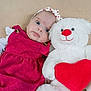 baby, infant, teddy_bear, stuffed_animal, red_heart, pink_dress, headband, portrait, lying_down, soft_toy, cute, big_eyes, plush, blanket, close_up, adorable, indoor, child, hand, smile