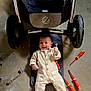baby, child, concrete_floor, cute, equipment, feet, hands, happy, indoors, infant, mat, mechanic_outfit, playful, repair, screwdrivers, smiling, stroller, tools, workshop, wrenches