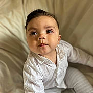 Ronald is registered to the contest to win money with this photo: baby, child, infant, white_shirt, pants, sitting, blanket, soft_texture, curious, portrait, indoors, cute, young_child, face, eyes, expression, natural_light, closeup, skin, person