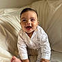baby, infant, child, smiling, happy, sitting, white_shirt, barefoot, indoors, couch, soft_furniture, curly_hair, cute, portrait, playful, young_child, skin, hand, foot, cozy