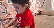 Luis is registered to the contest to win money with this photo: toddler, child, smartphone, couch, red_shirt, pacifier, indoor, blanket, floral_pattern, hand, foot, face, hair, screen, technology, furniture, living_room, person, seated, concentration