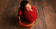 Niall is registered to the contest to win money with this photo: newborn, baby, sleeping, infant, portrait, red_blanket, swaddled, wicker_chair, basket, wooden_floor, indoors, peaceful, cozy, closed_eyes, black_hair, head, hands, newborn_photography, warm_lighting, adorable