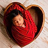 newborn, baby, sleeping, swaddled, red_blanket, heart_shaped_basket, wooden_basket, portrait, infant, peaceful, closed_eyes, hands, face, hair, indoor, wooden_floor, cozy, rustic, photography, red