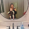 baby, bathroom, black_clothing, cleaning, curtain, door, front_carrier, light_switch, mirror, person, reflection, selfie, short_hair, sink, smile, soap_dispenser, towel, white_wall, window, woman