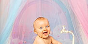 Milo a rejoint le concours — aidez-le/la à gagner de superbes lots ! baby, child, tub, faucet, pastel_colors, blue_eyes, smiling, indoor, soft_light, fabric, rainbow, playful, cute, portrait, happy, infant, sitting, whimsical, colorful, fun