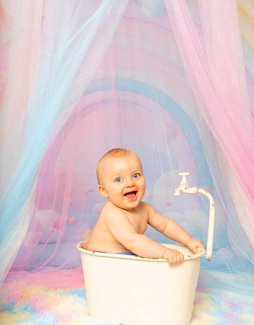 Milo a rejoint le concours — aidez-le/la à gagner de superbes lots ! baby, child, tub, faucet, pastel_colors, blue_eyes, smiling, indoor, soft_light, fabric, rainbow, playful, cute, portrait, happy, infant, sitting, whimsical, colorful, fun