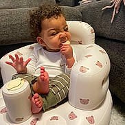 Navari joined the competition — help win amazing prizes! baby, child, curly_hair, inflatable_chair, teddy_bear_pattern, snack, bite, funny_face, living_room, couch, carpet, white_clothing, green_pants, bare_feet, indoor, cute, infant, seated, playful, cozy