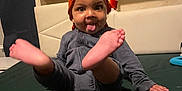 Navari is registered to the contest to win money with this photo: toddler, child, orange_headwrap, tongue_out, bed, dark_green_bedspread, playful, indoor, person, cute, happy, smiling, legs_up, headwear, clothing, furniture, home, portrait, young_child, sitting