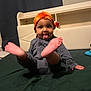 toddler, child, orange_headwrap, tongue_out, bed, dark_green_bedspread, playful, indoor, person, cute, happy, smiling, legs_up, headwear, clothing, furniture, home, portrait, young_child, sitting