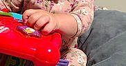 Clairissa is registered to the contest to win money with this photo: baby, child, infant, smiling, portrait, sitting, toy, ride_on_toy, colorful, pink_outfit, floral_clothing, indoors, bedroom, bedding, cozy, face, hands, playtime, happy, photograph