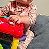 baby, child, infant, smiling, portrait, sitting, toy, ride_on_toy, colorful, pink_outfit, floral_clothing, indoors, bedroom, bedding, cozy, face, hands, playtime, happy, photograph